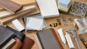 Wood, acrylic, metal, foam, fabric, resin samples, fasteners, adhesive tubes, calipers, and a utility knife arranged on a maker bench.